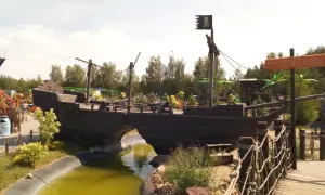 Statek piracki z czarną banderą i armatami, jak z krainy Canpol Wonderland, przecina wodny rów.