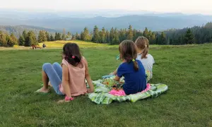 Trzy dziewczynki siedzą na kocu na trawie, podziwiając rozległy widok na Beskid Żywiecki.