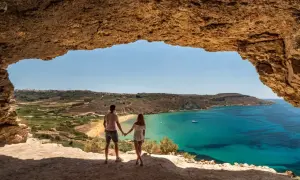 Para Malta zabierz lekkie, zwiewne ciuchy. Para podziwia widok na turkusowe morze i plażę z jaskini.