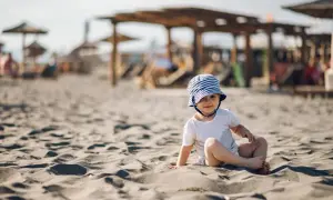 Uroczy maluch w kapelusiku na plaży. Idealne miejsce, gdzie na wakacje z rocznym dzieckiem.