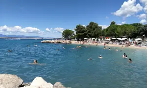 Crikvenica atrakcje: plaża pełna ludzi kąpiących się i opalających, błękitne morze, zielone drzewa i góry w tle.