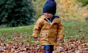 Mały chłopiec w jesiennej kurtce i czapce spaceruje po parku pełnym liści. Idealne miejsce, gdzie na weekend z dzieckiem jesienią.