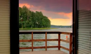 Drewniany pomost z widokiem na jezioro i las o zachodzie słońca.