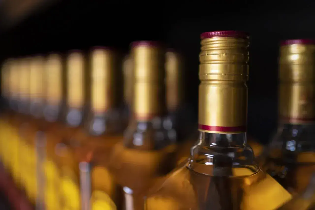 Rząd butelek z alkoholem, przypominający o limitach w Islandii. Złote zakrętki i bursztynowy płyn.