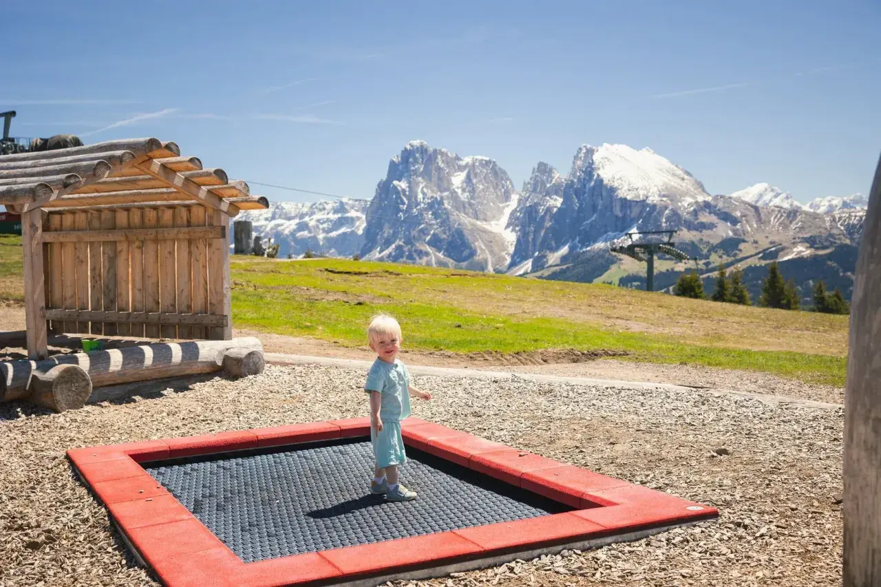 Mały chłopiec cieszy się zabawą na trampolinie na tle majestatycznych Dolomitów.