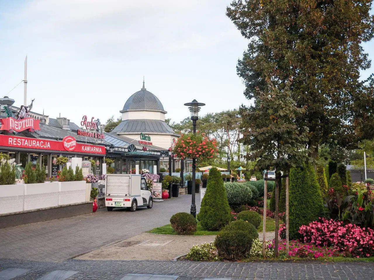 Ulica w Międzyzdrojach z restauracjami i kawiarniami, zielenią i ozdobnymi krzewami. Idealne miejsce na spacer i odkrywanie międzyzdrojskich atrakcji.