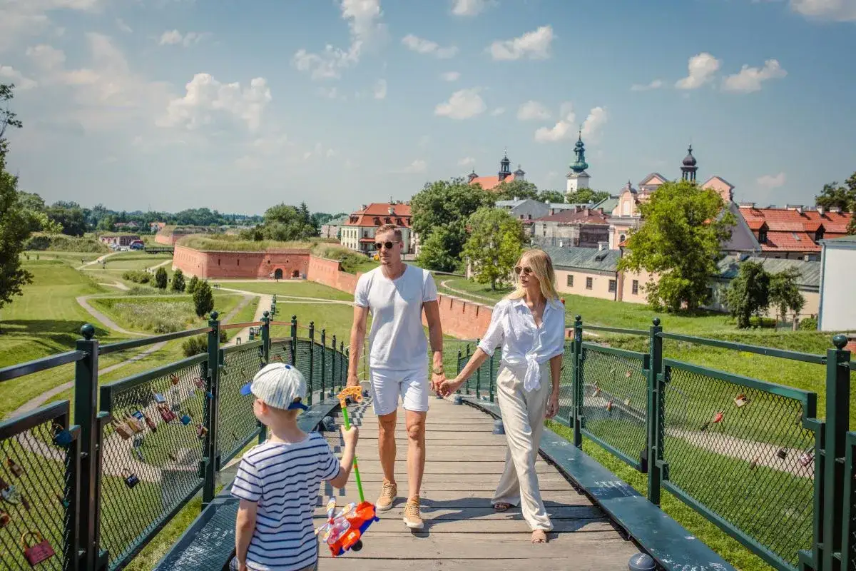 Rodzina spaceruje po moście z widokiem na zabytkowe fortyfikacje. Wspaniałe atrakcje dla dzieci lubelskie czekają!