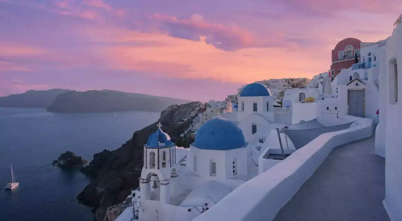 Zachód słońca nad Santorini, jednym z najpiękniejszych wysp greckich. Białe domy z niebieskimi kopułami kościołów na tle różowego nieba.