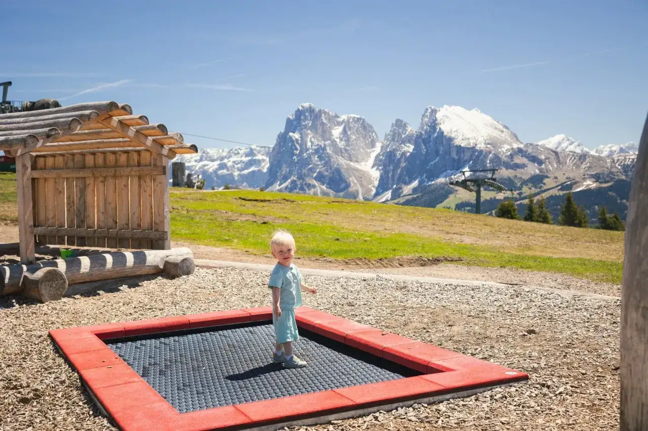 Mały chłopiec cieszy się trampoliną na tle majestatycznych Dolomitów.