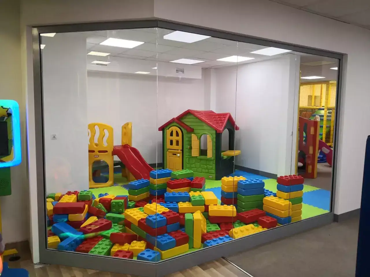 Kolorowa sala zabaw dla niemowląt z domkiem, zjeżdżalnią i wielkimi klockami.