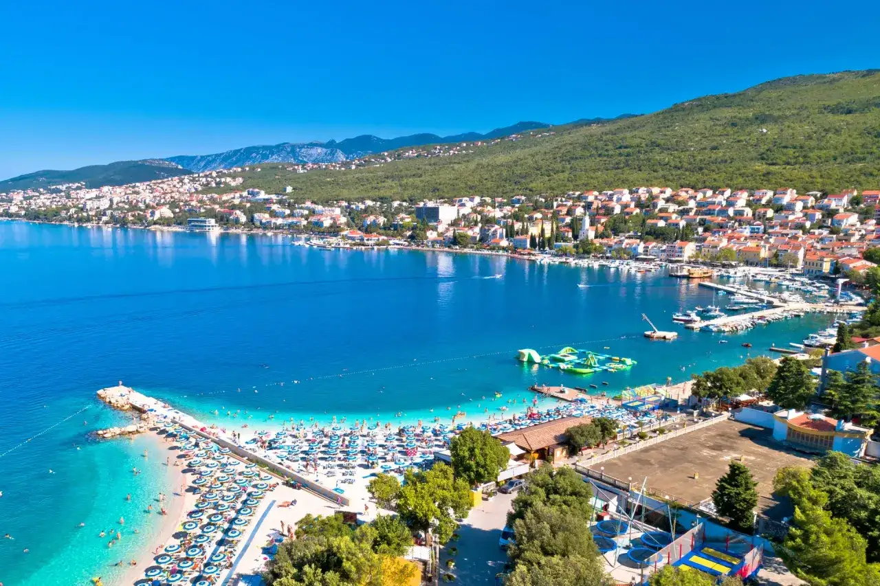 Crikvenica atrakcje: słoneczna plaża z leżakami, wodny park rozrywki i zatoka pełna łodzi.