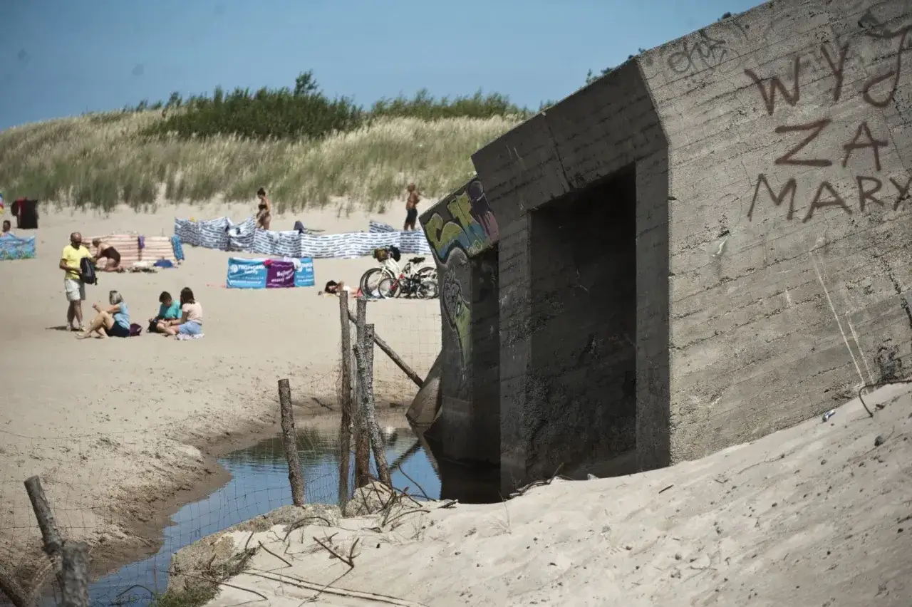 Betonowy bunkier na plaży, obok rower i ludzie odpoczywający na piasku. To jedne z wielu atrakcji dla dzieci w Bobolinie.