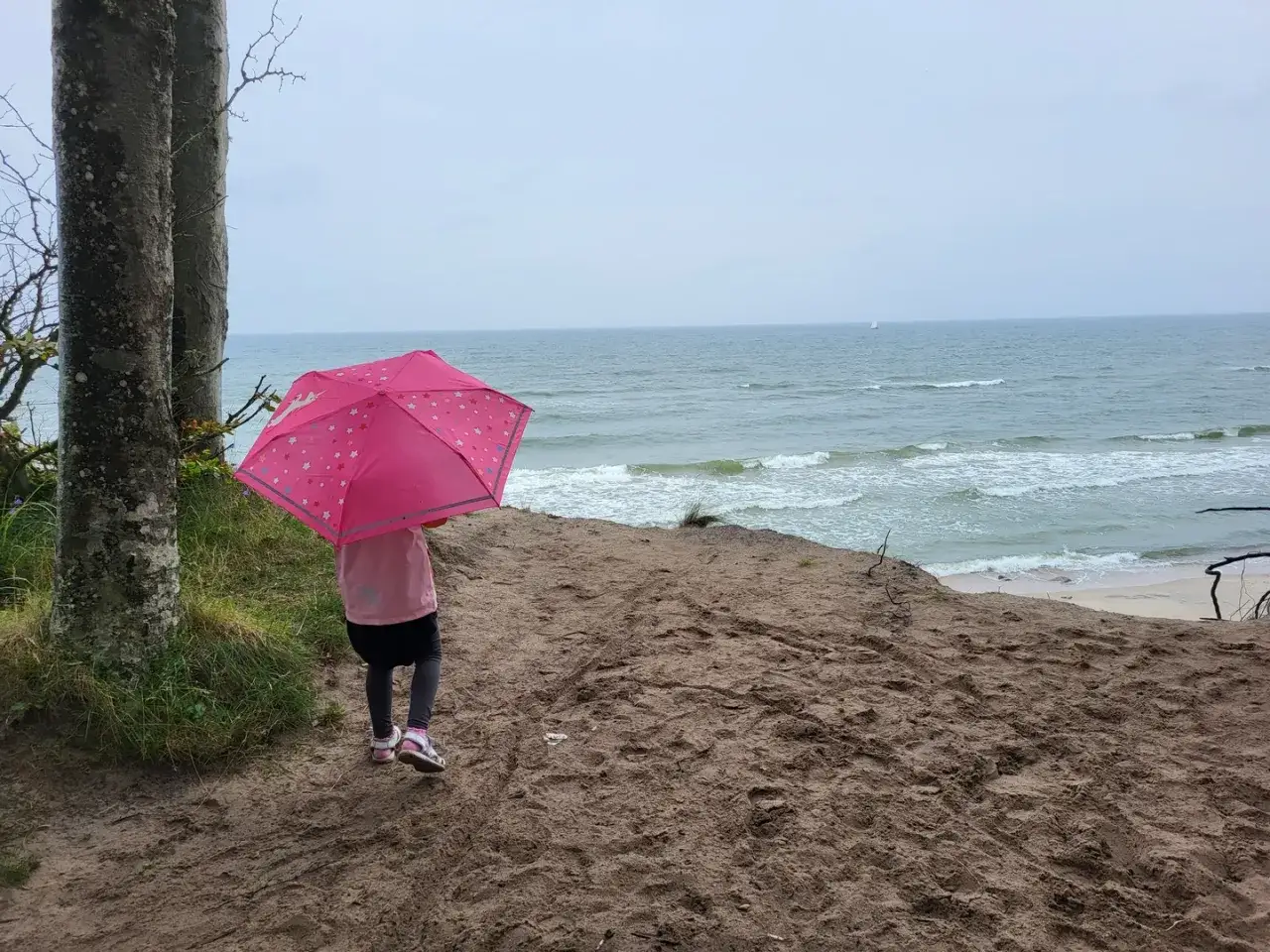 Dziewczynka z różowym parasolem na klifie. Morze i plaża tworzą wspaniałe rowy atrakcje dla dzieci.