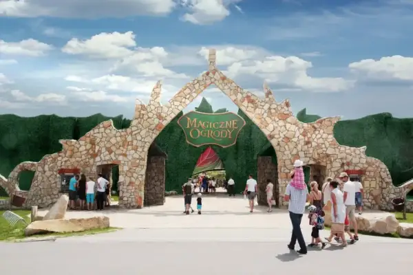 Kamienna brama z napisem "Magiczne Ogrody" zaprasza do niezwykłych atrakcji turystycznych. Rodziny wchodzą do bajkowego świata.