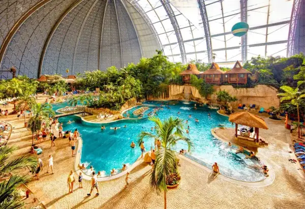 Tropikalny raj w aqua parku w Berlinie. Ludzie kąpią się w basenie wśród palm i egzotycznej roślinności pod ogromną kopułą.